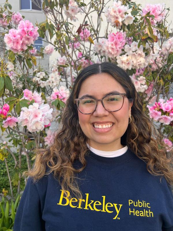Sofia Ledesema smiles while wearing a UC Berkeley Public Health sweatshirt in front of pink flowers. 